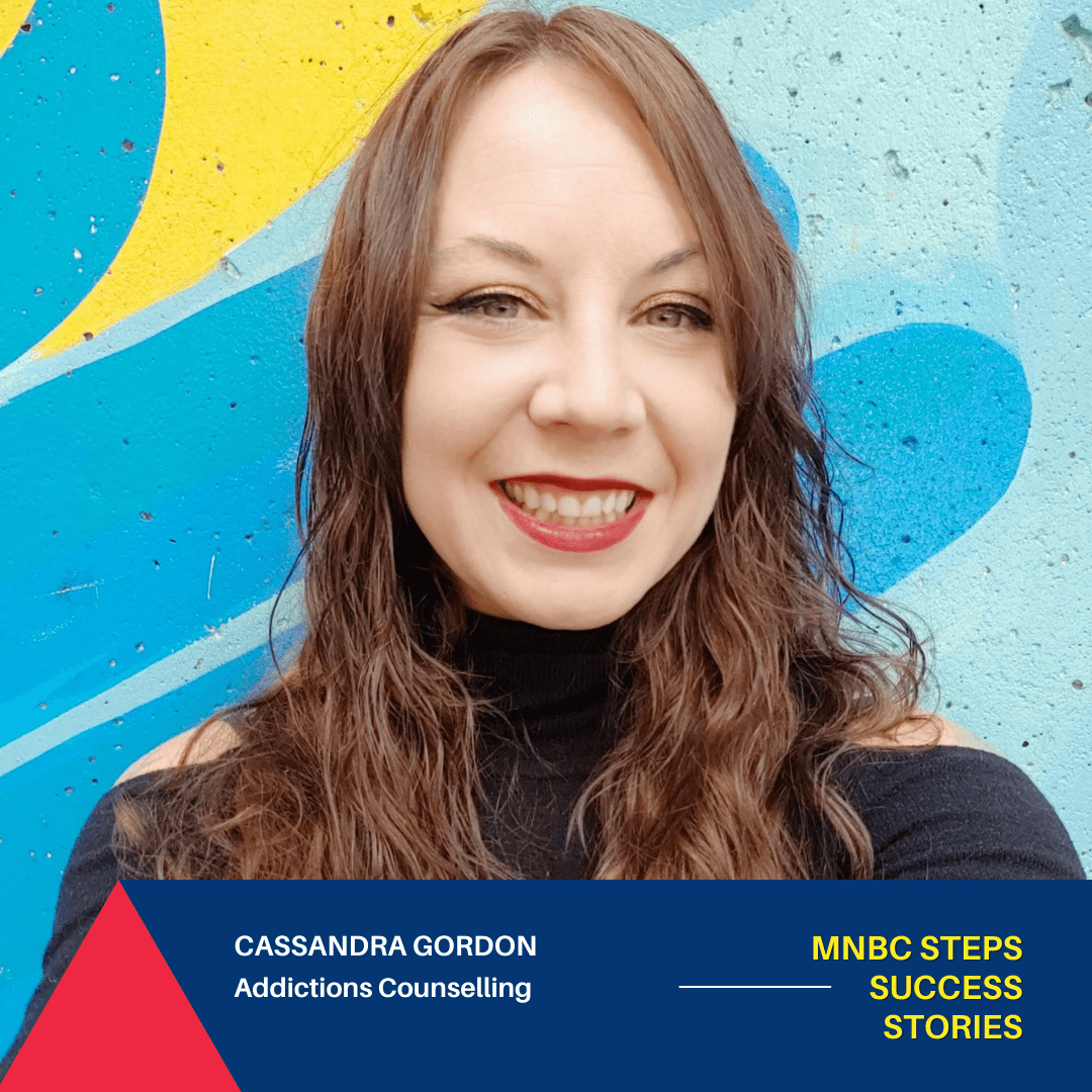 Cassandra Gordon smiles directly at the camera in front of a brightly coloured wall.