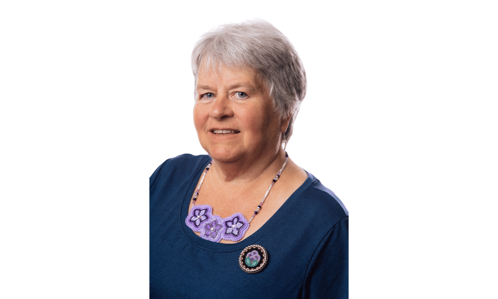 Headshot of a woman in a dark shirt with a beaded necklace.