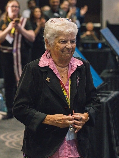 A smiling elderly woman in a black jacket.