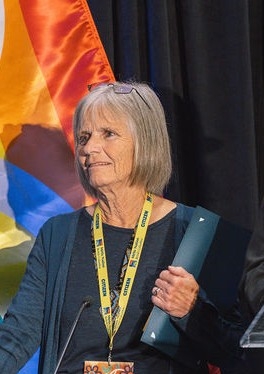 A woman stands by a podium holding a folder.