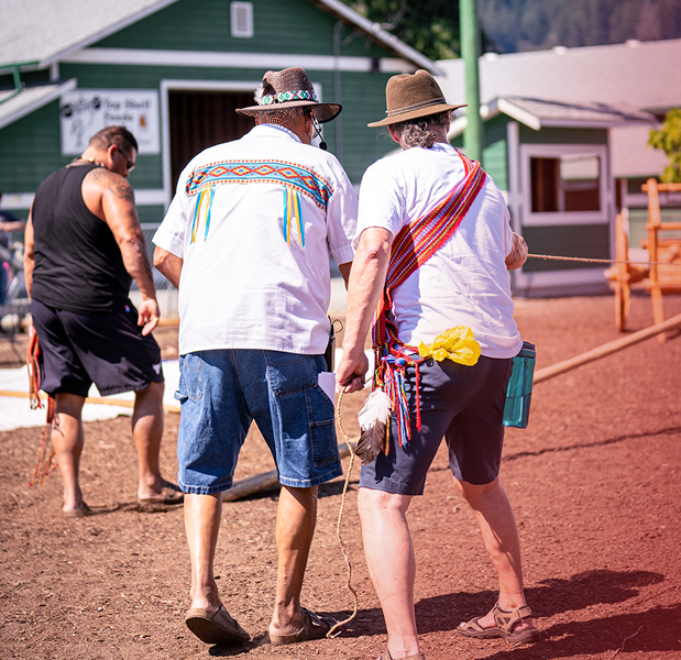 Two men are talking: the man on the left is wearing a beaded Métis shirt, and the man on the right is wearing a traditional Métis sash.