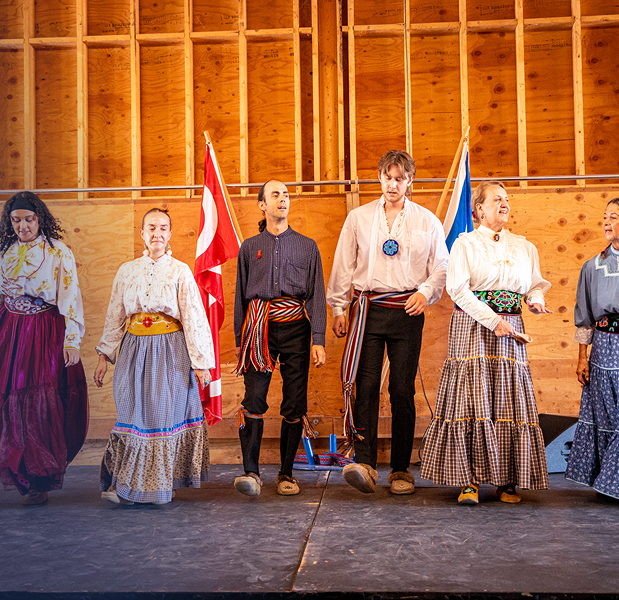 A group of men and women wearing traditional Métis clothing standing in a row.
