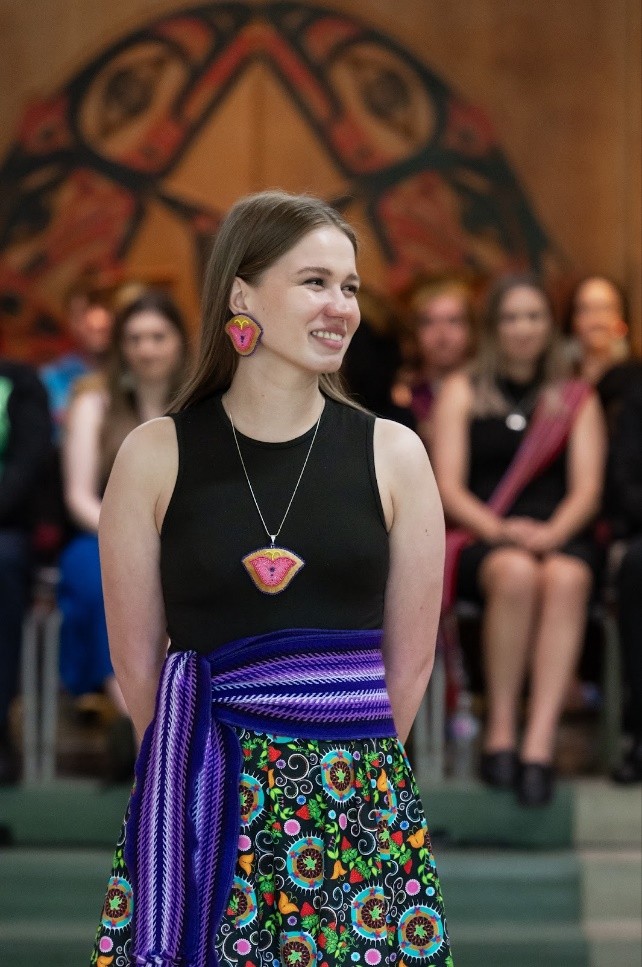 Brynn McKenna is smiling in a black tank top with a purple Métis sash around her waist in front of a crowd.