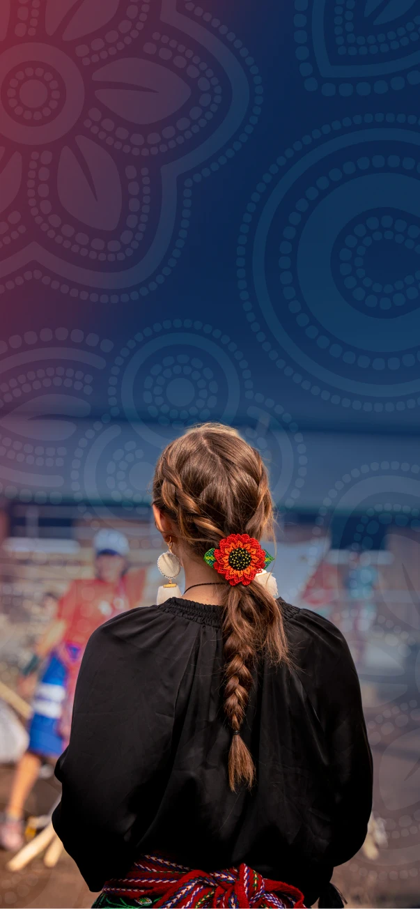 A woman with a braided hairstyle and colorful floral hair accessory stands at an outdoor cultural event.
