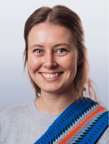 Danielle Bergevin is smiling in a grey shirt with a blue- and orange-coloured Métis youth sash.