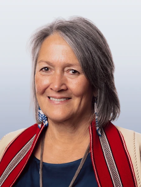 Debra Fisher is smiling in a black shirt with a red Métis sash draped over her shoulders against a white background.