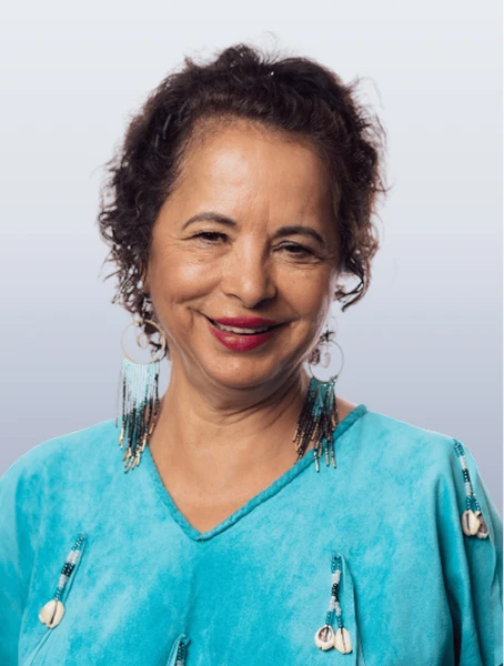Paulette Flamond is smiling in a blue shirt with hanging beaded shells against a neutral background.