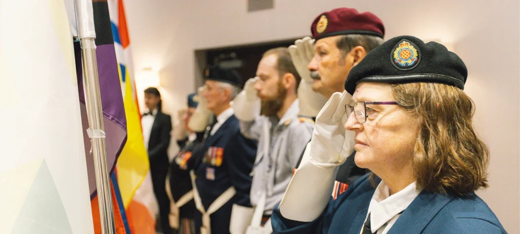 A group of Métis veterans in uniform standing in front of flags.