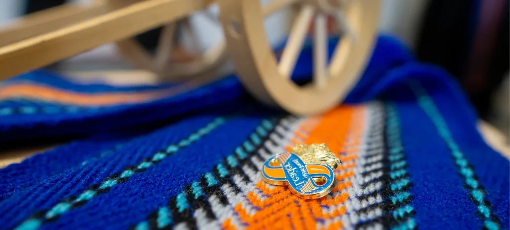 An enamel pin that says “Métis Youth Leader” on a traditional Métis youth sash.